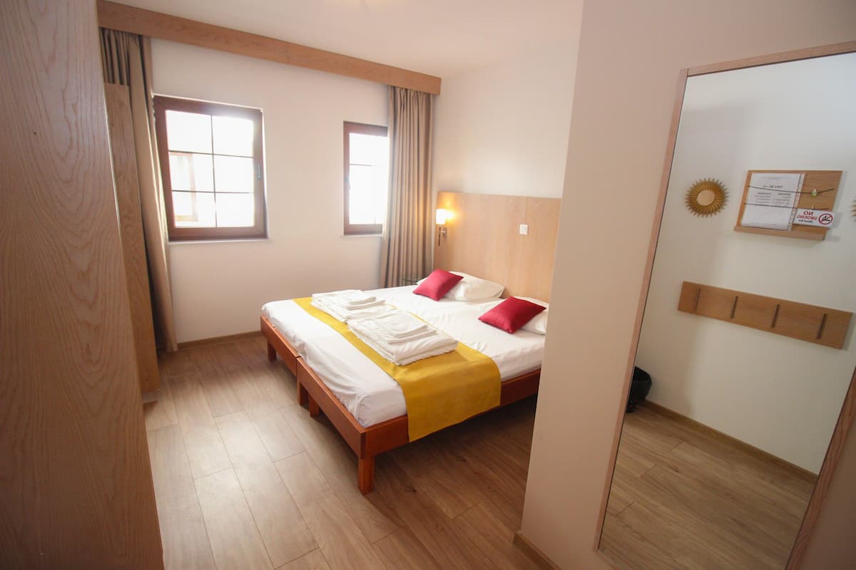 Habitación de hotel con una cama de madera, una colcha amarilla y un espejo en una pared.