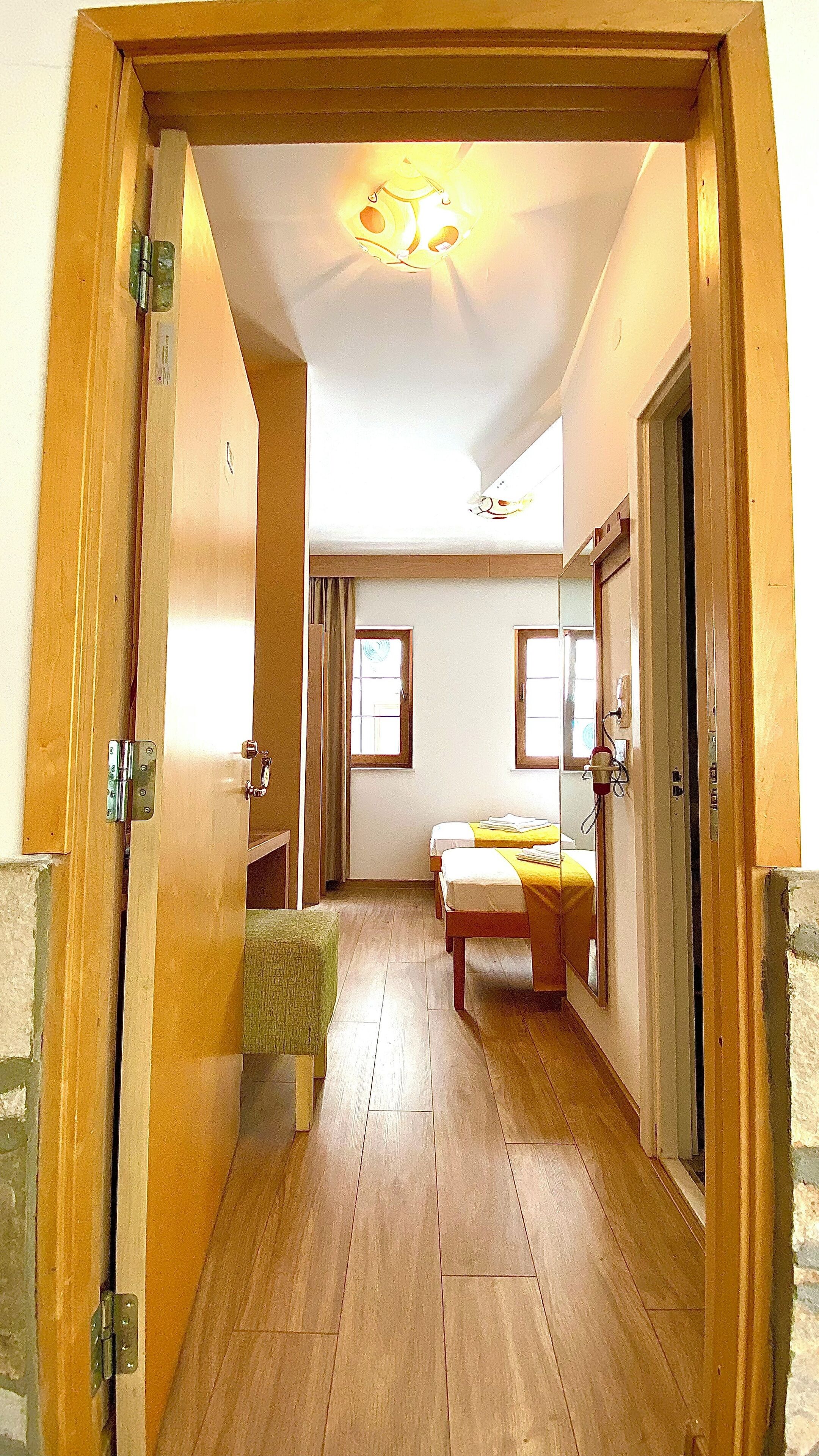A narrow hallway leading to a bedroom with a bed, a small stool, and a window.