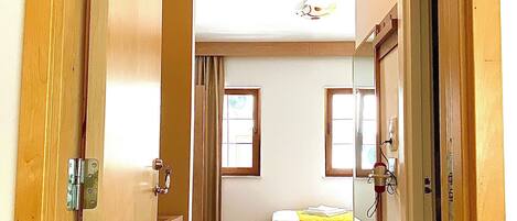 A narrow hallway leading to a bedroom with a bed, a small stool, and a window.
