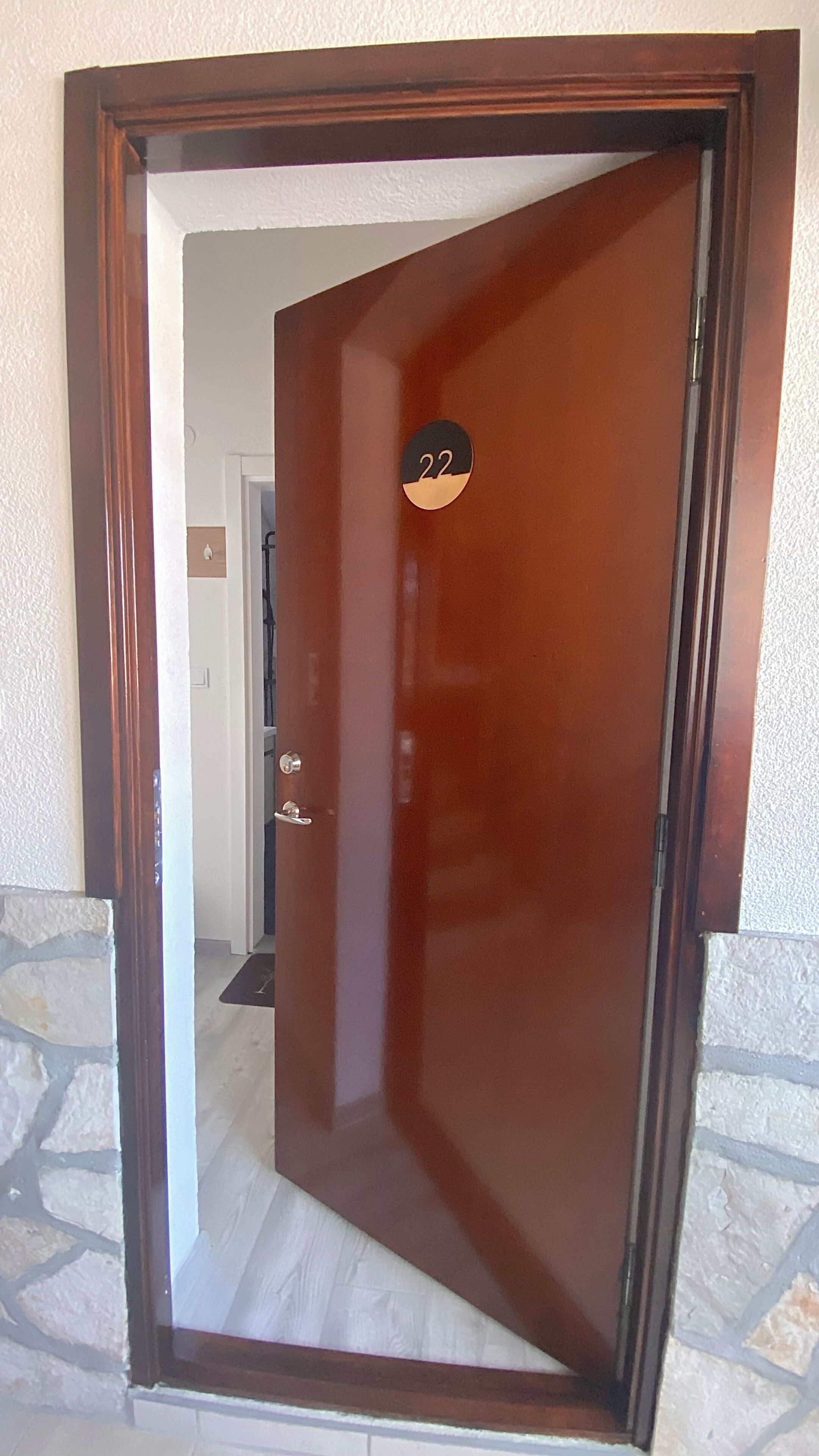Une porte en bois avec une plaque portant un numéro, un mur en pierre et un sol carrelé.
