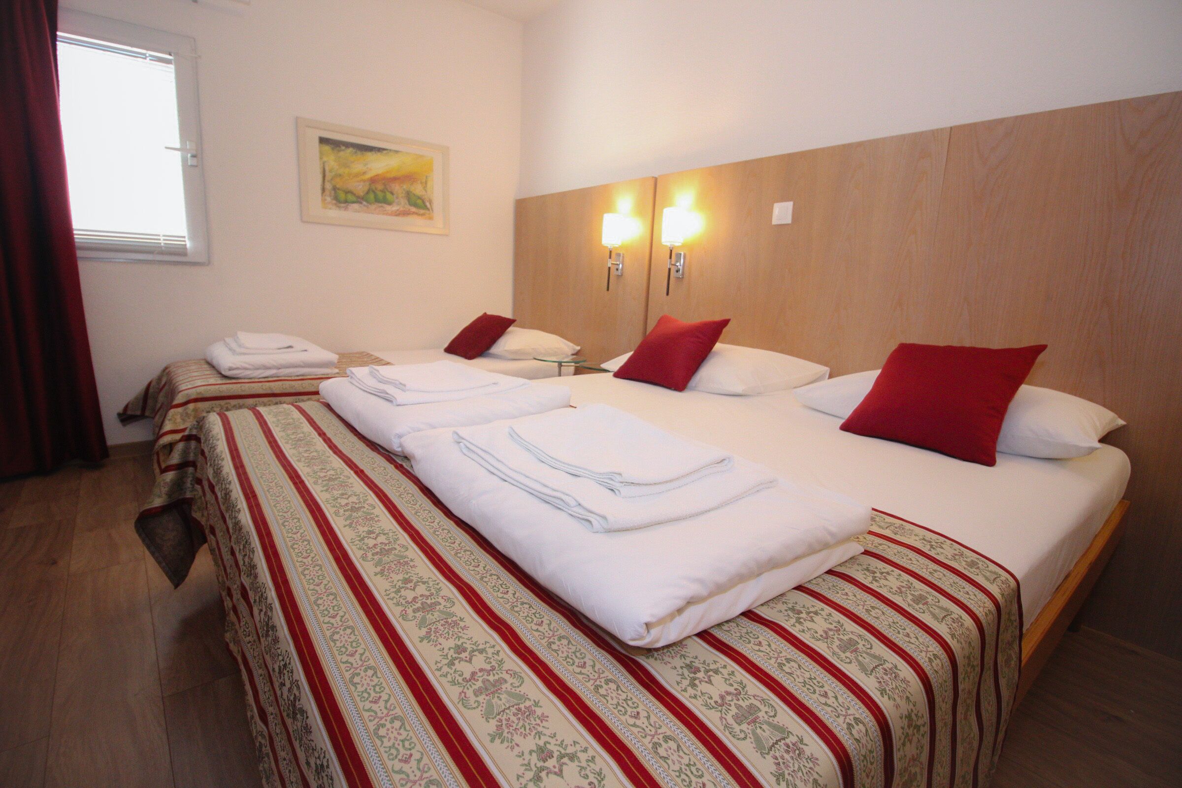 Quarto de hotel com duas camas, cabeceira de madeira e duas luzes fixadas na parede.