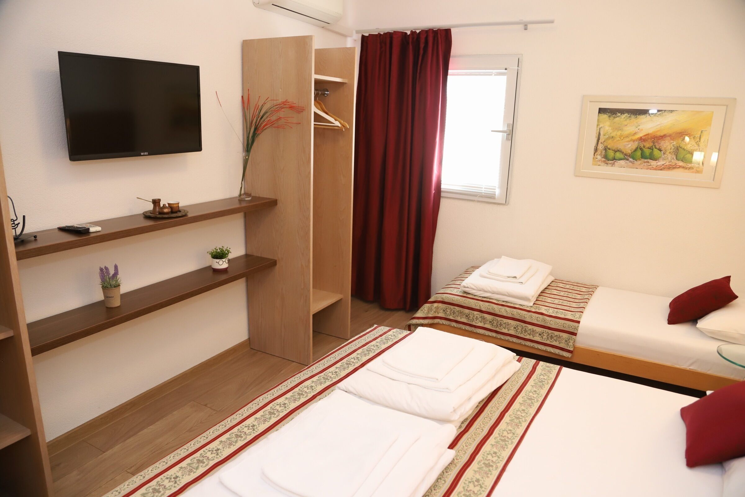 A hotel room with a bed, a TV, a wardrobe, and a painting on the wall.