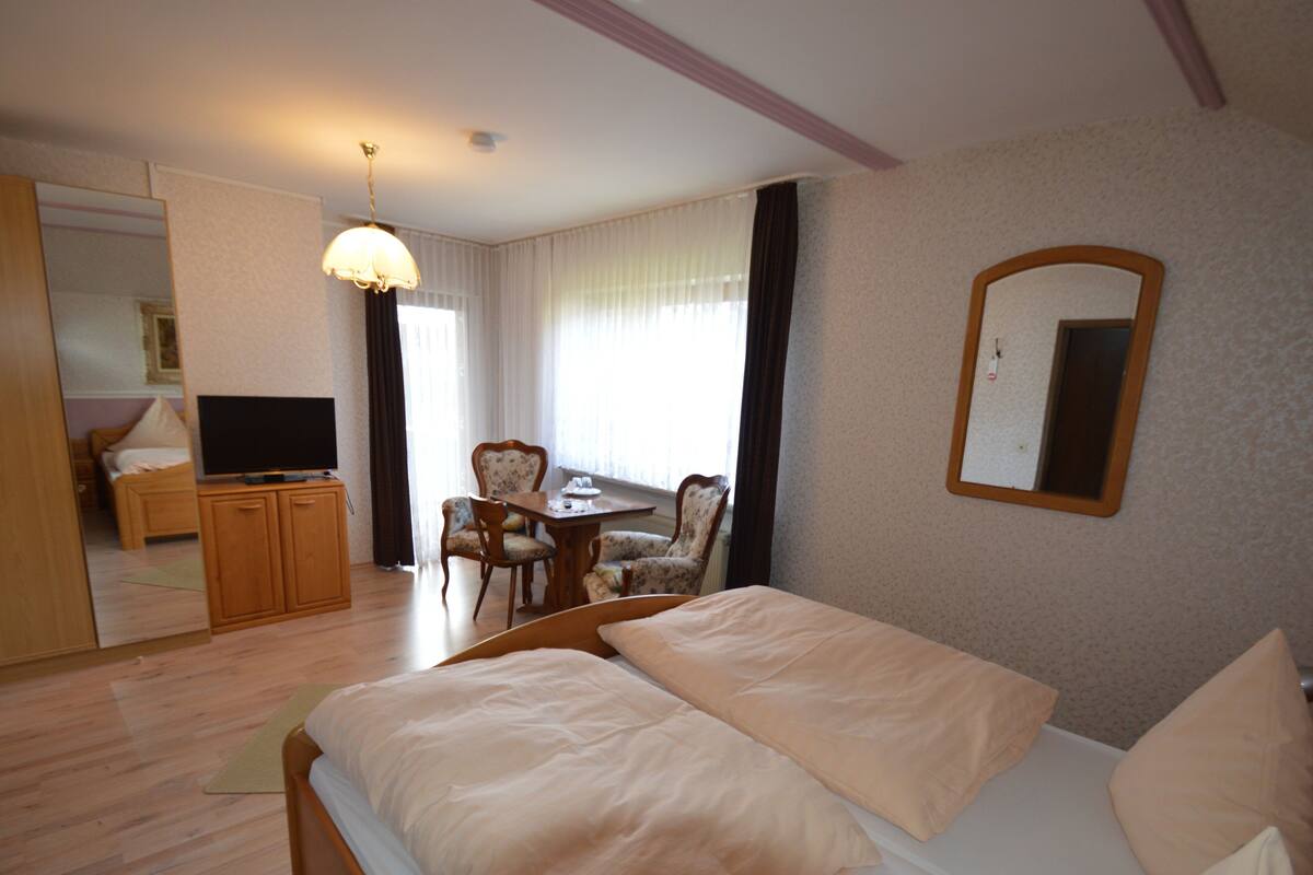 A hotel room with a bed, a desk, a chair, a television, and a mirror.