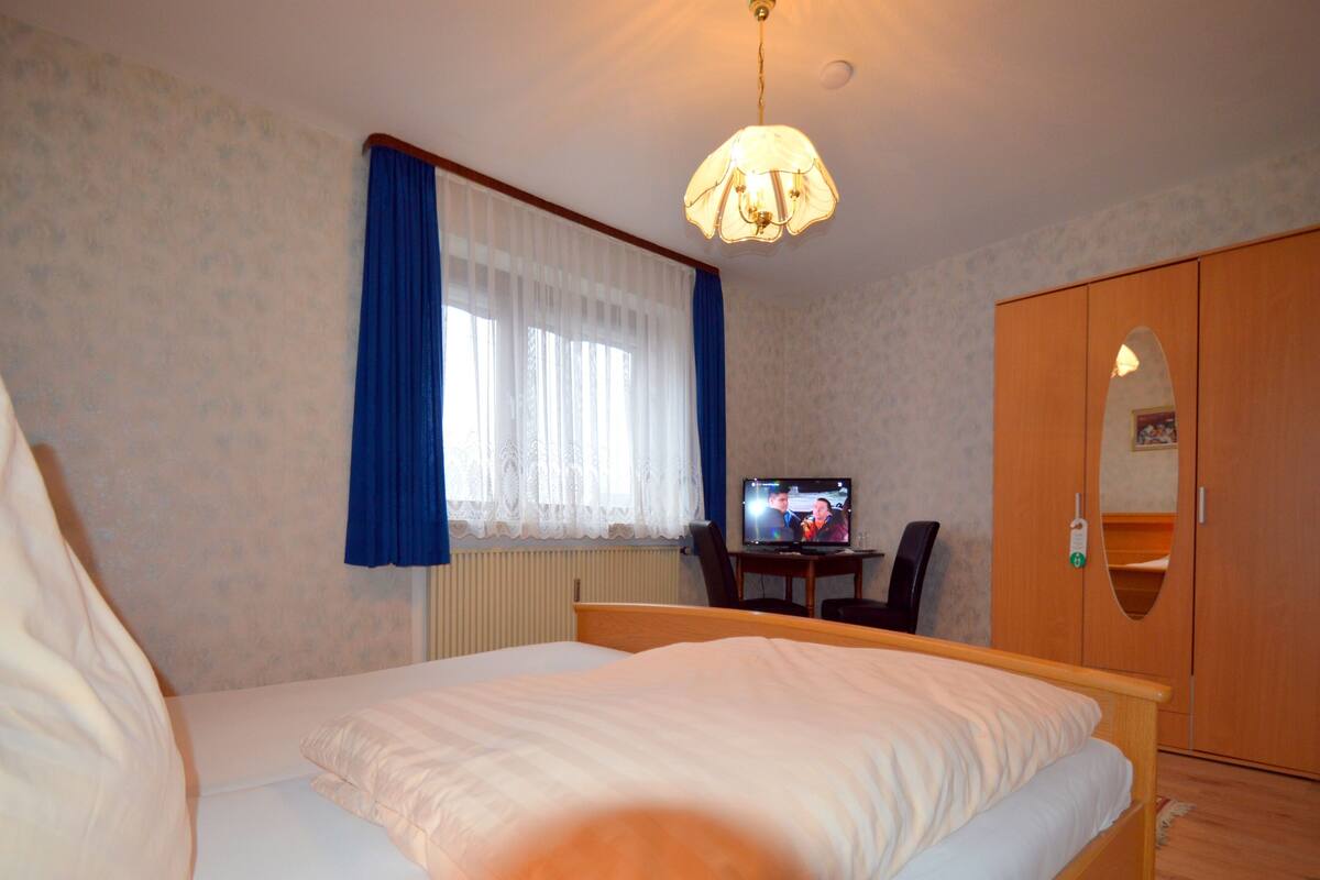 A hotel room with a bed, a desk with a computer, a wardrobe, and a window with curtains.