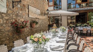 A long dining table set with white tablecloths, glassware, and floral centerpieces, surrounded by wicker chairs. - Hotel Nou Romà (Denia)
