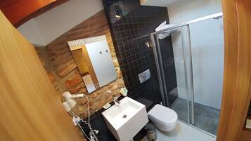 Un baño con pared de piedra, un lavamanos blanco, un inodoro y cabina de ducha con mampara de cristal.