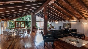 A spacious living area with wooden flooring, a black leather sofa, and a coffee table. Large windows provide natural light and a view of greenery outside. - Hotel Nou Romà (Denia)