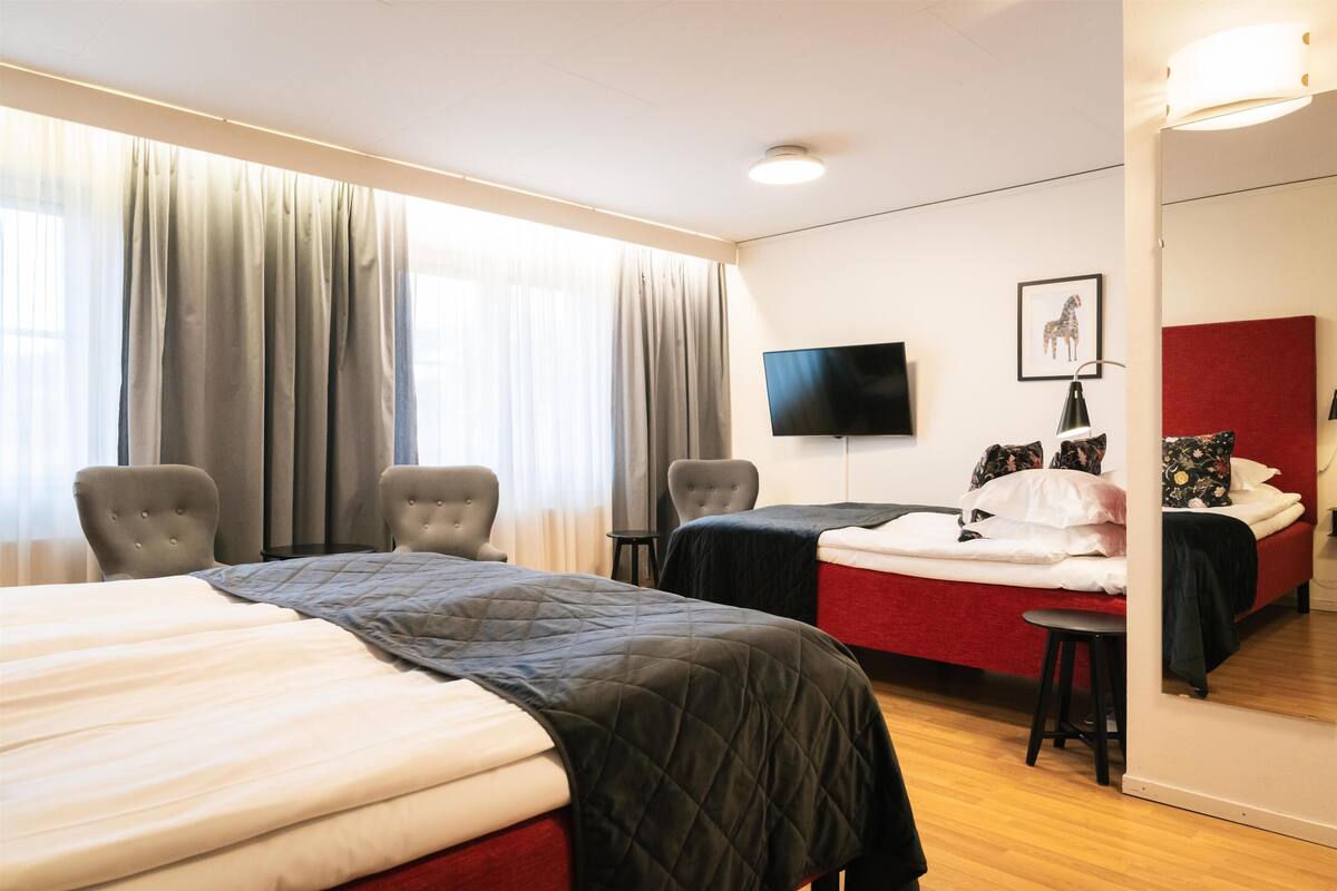 A hotel room with two beds, a TV, a mirror, and a window with curtains.