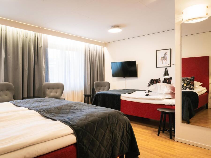 Quarto de hotel com duas camas, televisão, espelho e janela com cortinas.