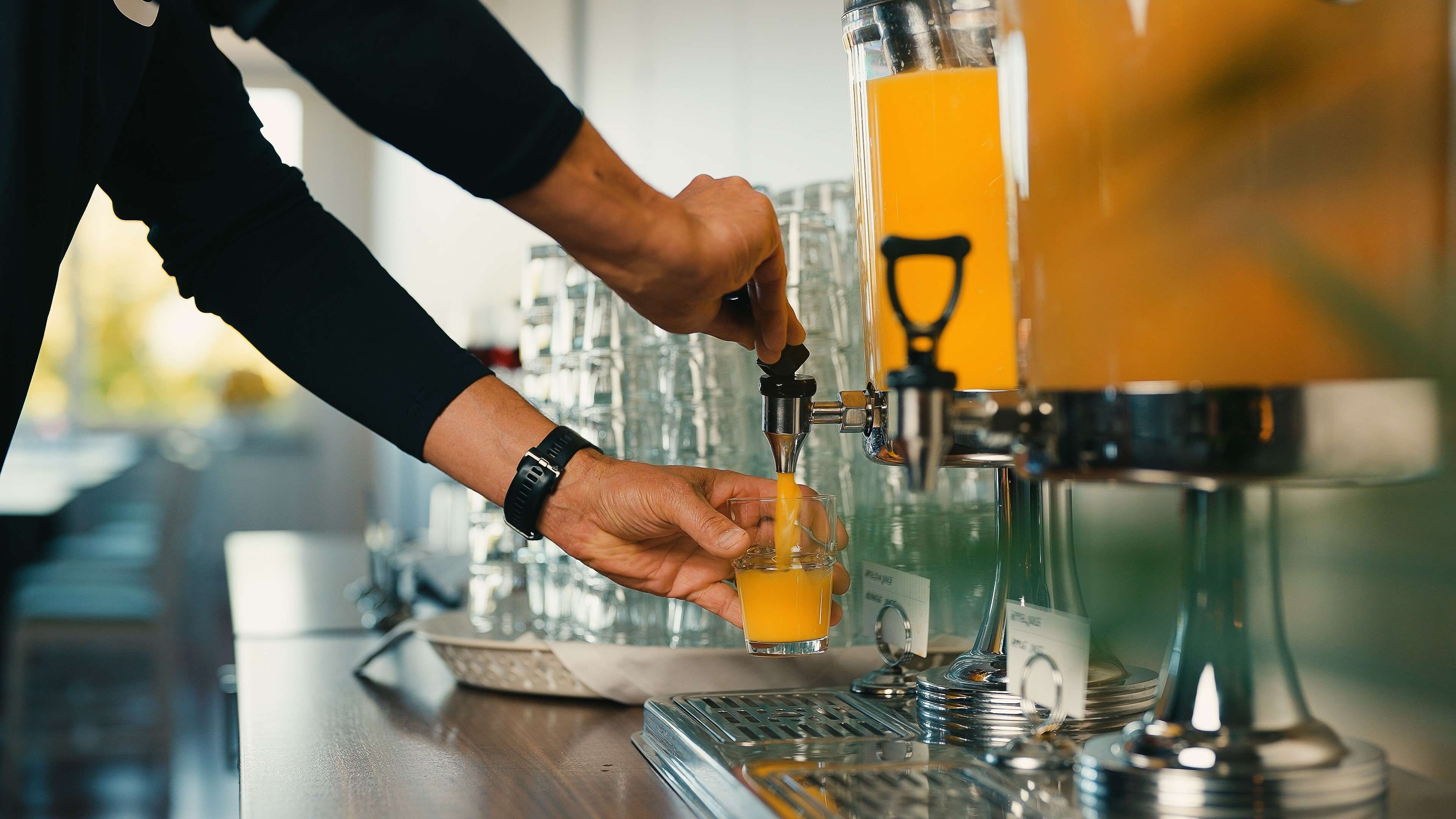 Iemand schenkt sinaasappelsap uit een kraan in een glas.