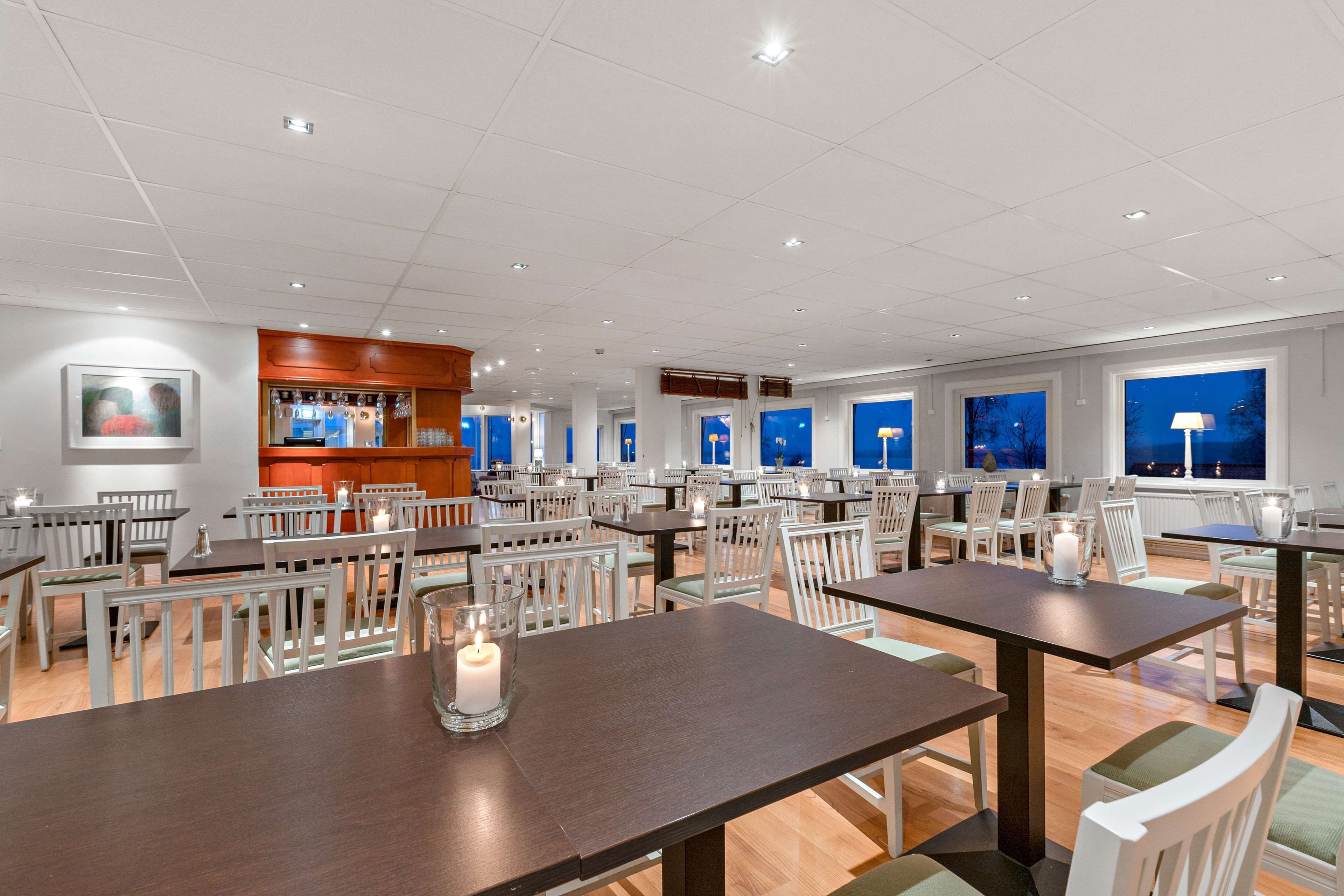 Un restaurante espacioso con varias mesas y sillas, una zona de bar y grandes ventanales que ofrecen vistas al cielo nocturno.