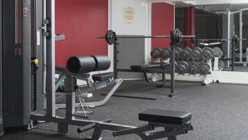 Un gimnasio con equipo de levantamiento de pesas, una banca y un espejo fijado a la pared.