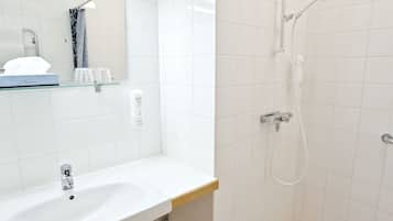 A bathroom with a white sink, a mirror, a shower, and a glass shelf with toiletries.