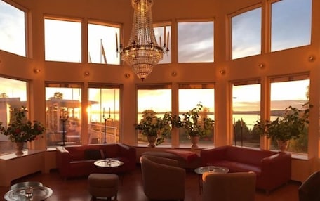 A spacious room with large windows, a chandelier, and red sofas.