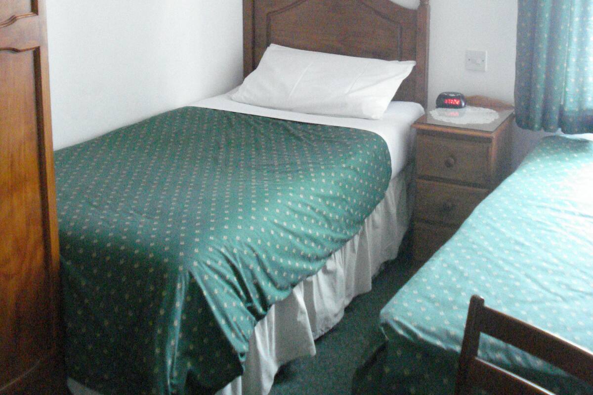 A small, single-bed room with a wooden headboard, a bedside table with a clock, and a nightstand.