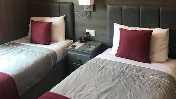 A hotel room with two beds, a nightstand with a clock, and a modern chandelier. - Masslink Guest House (Horley)