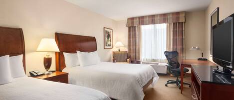 A hotel room with two beds, a desk with a computer, a TV, and a window with curtains.