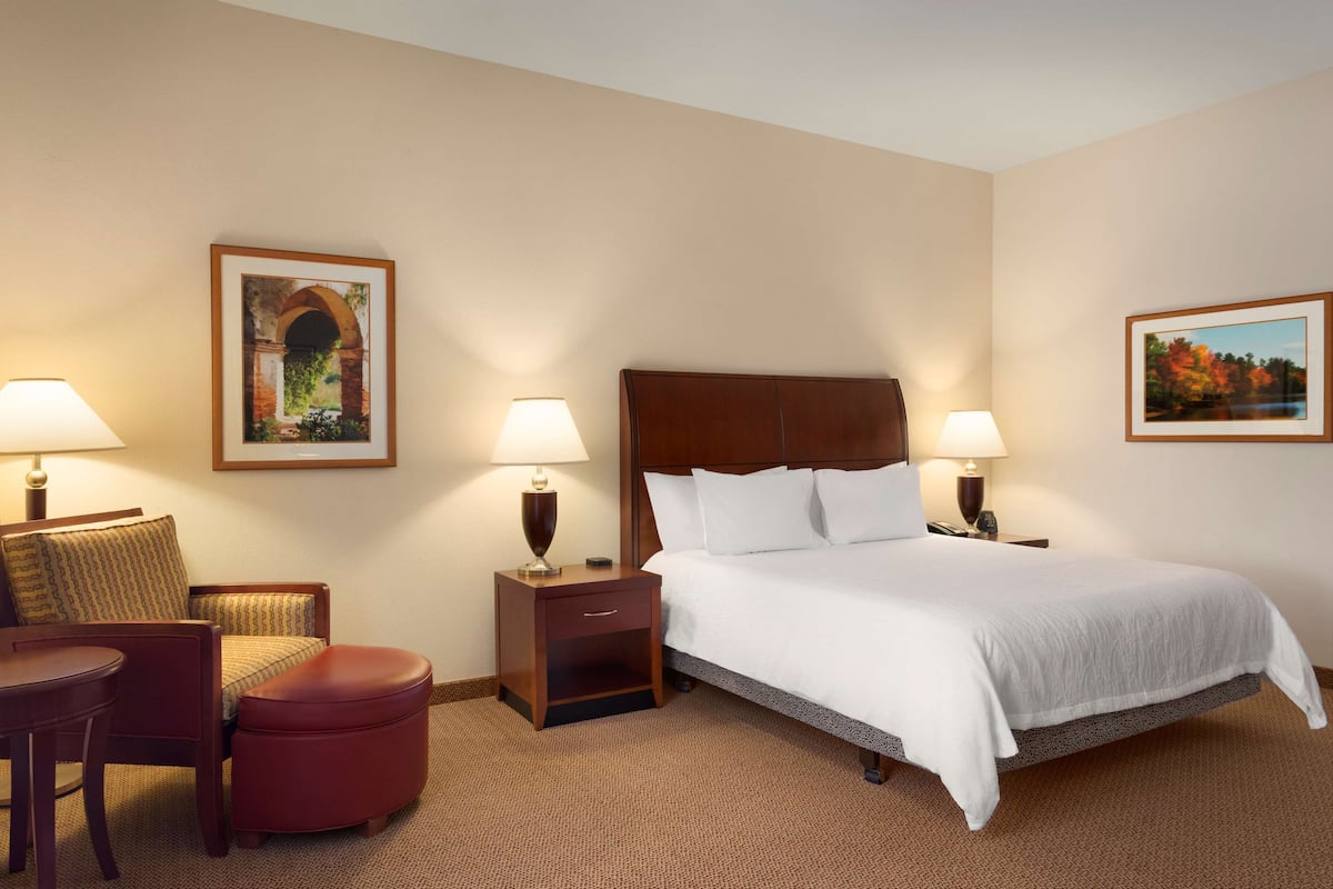 A hotel room with a large bed, two bedside tables with lamps, a chair, and a small ottoman.