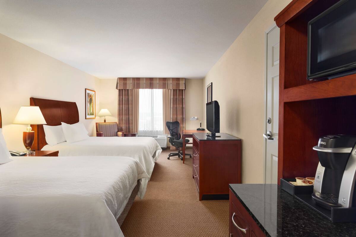 A hotel room with two beds, a desk, a chair, a television, and a coffee maker.