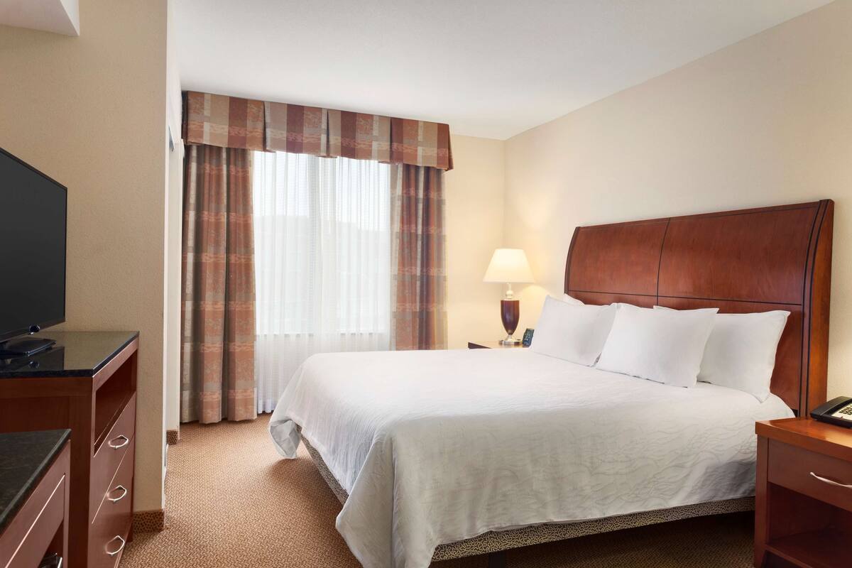 A hotel room with a large bed, a TV, a desk, and a lamp.