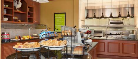 A hotel kitchen with a buffet setup, including bread, pastries, and a variety of breakfast items.