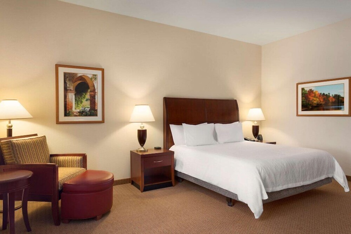 A hotel room with a bed, two nightstands, a chair, a small table, and two lamps.