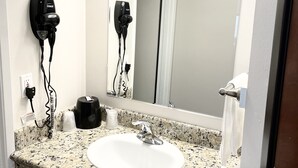 A bathroom with a granite countertop sink, a mirror, a hairdryer, and a towel rack. - Dunes Motel Hillsboro (Hillsboro)