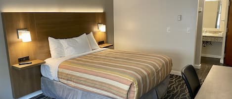 Una habitación de hotel con cama, mesitas de noche, escritorio y baño visible a través de una puerta abierta.