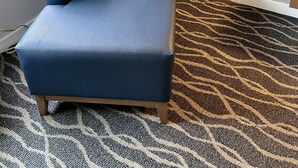 A corner room with a dark blue upholstered armchair, a patterned carpet, and a plain wall. - Dunes Motel Hillsboro (Hillsboro)