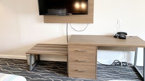A hotel room with a wooden desk, a flat-screen TV mounted above it, a telephone, and a patterned carpet. - Dunes Motel Hillsboro (Hillsboro)