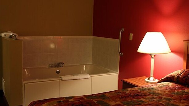 Et hotelværelse med badekar, et natbord med lampe og en seng med et farverigt tæppe.