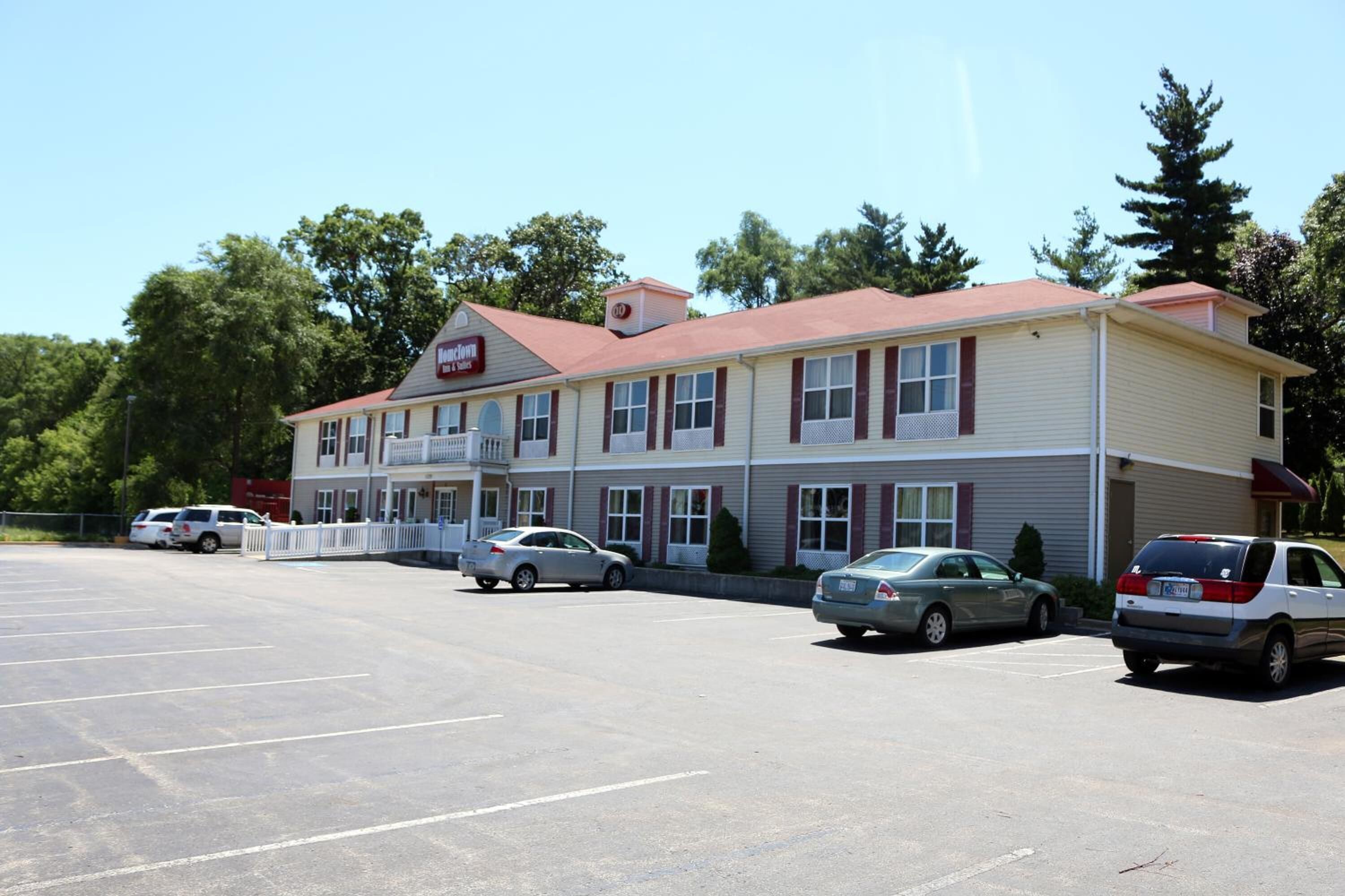 A two-story building with a red roof and beige walls, featuring a parking lot with several cars.