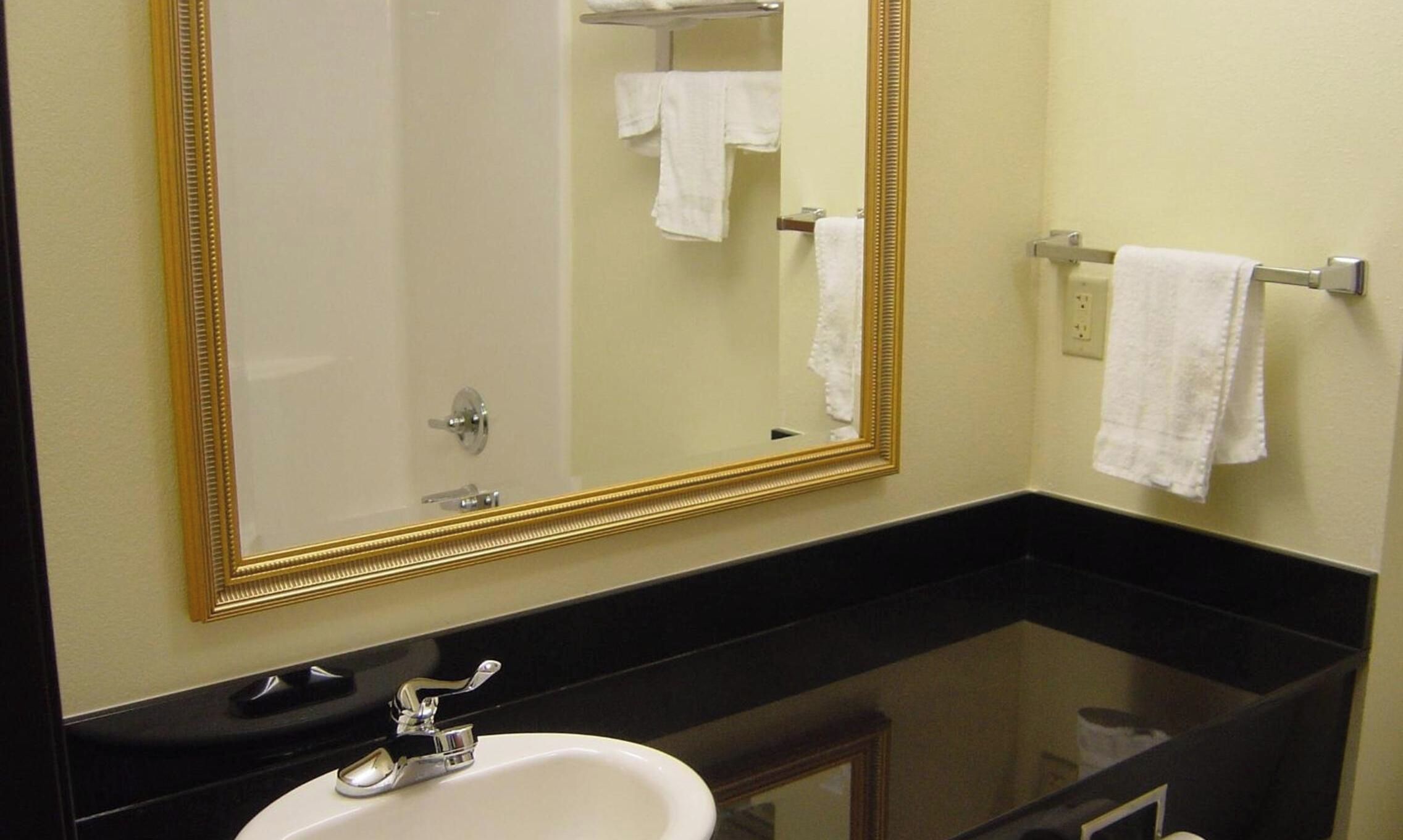 Un baño con un espejo grande, un lavamanos y dos toallas colgadas en toalleros.