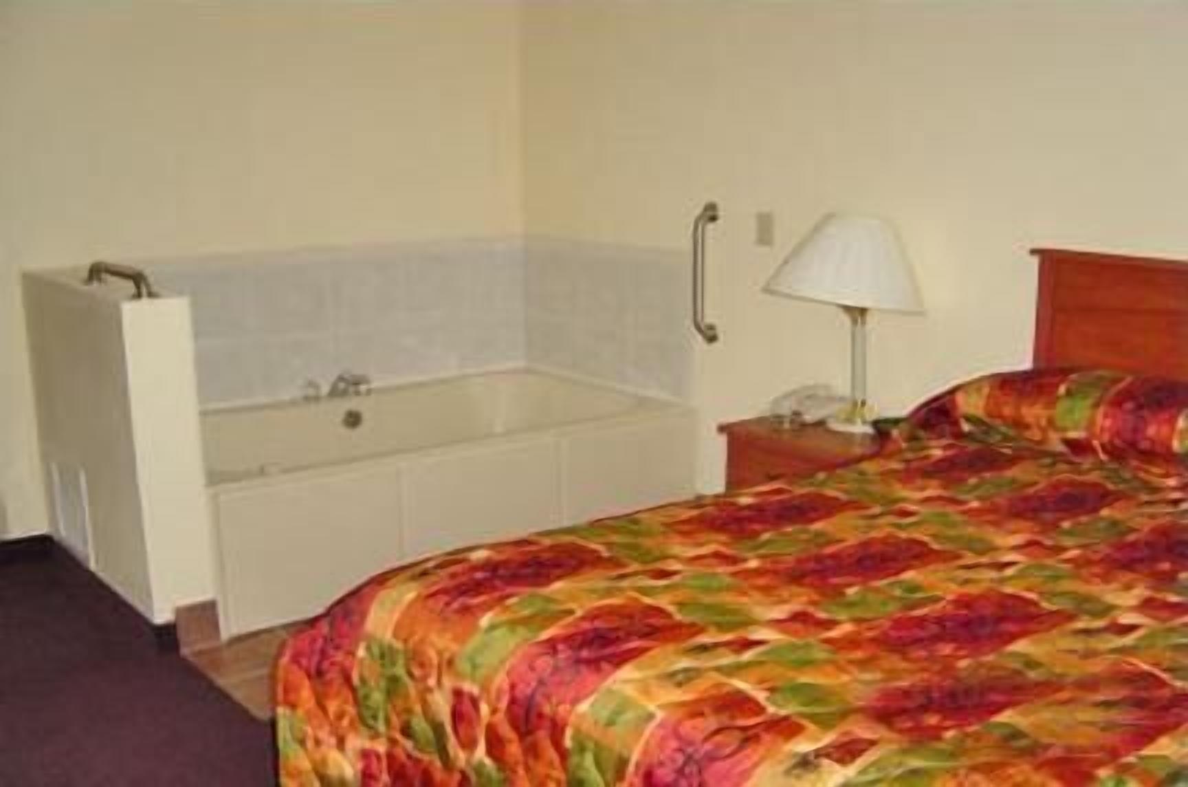 A hotel room with a single bed, a nightstand, a lamp, and a bathtub.