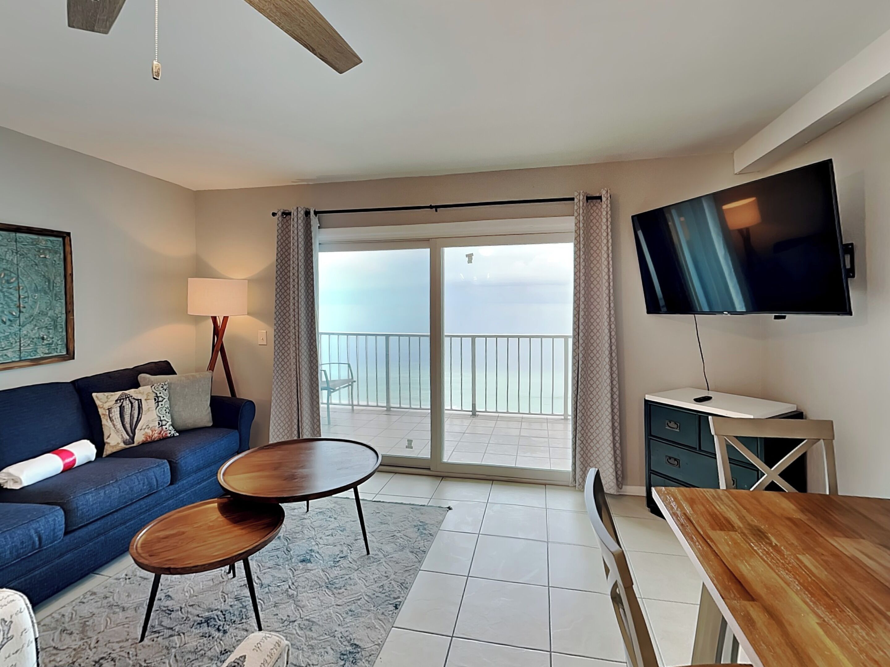 A modern living room with a sofa, two side tables, a TV, and a balcony with a view.