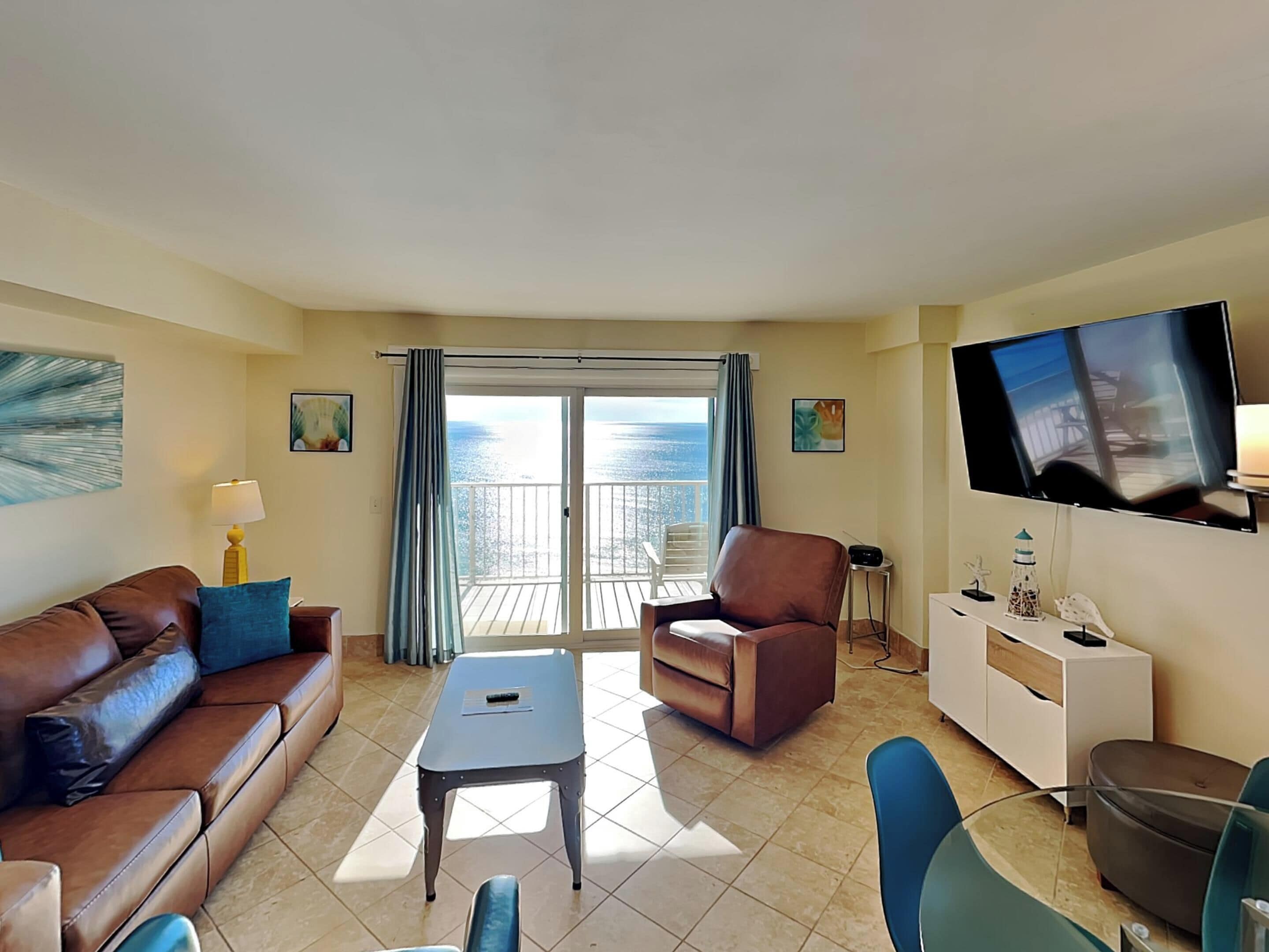 Un salon comprenant un canapé, un fauteuil, une télévision et un balcon avec vue sur la mer.