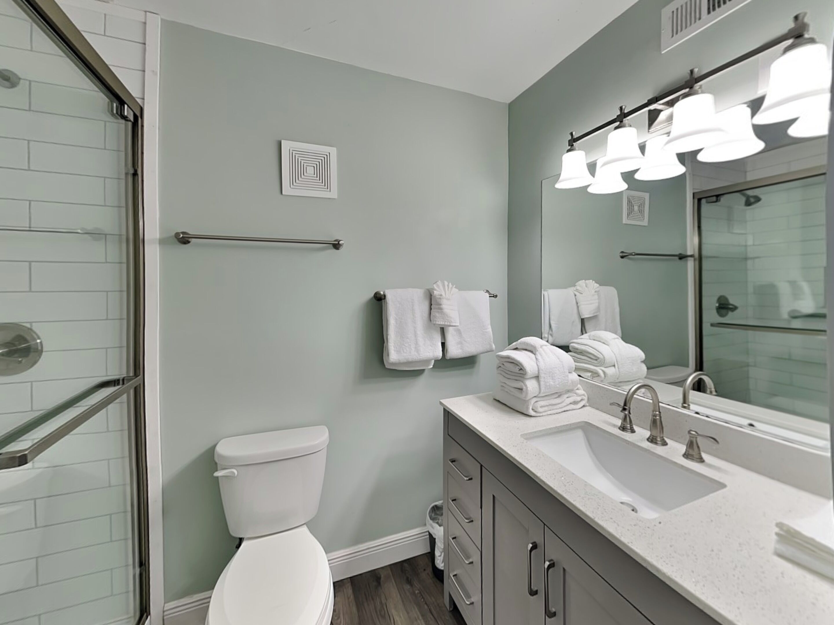 A modern bathroom with a glass shower enclosure, a white toilet, a sink with a mirror, and a towel rack.