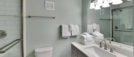 A modern bathroom with a glass shower enclosure, a white toilet, a sink with a mirror, and a towel rack.