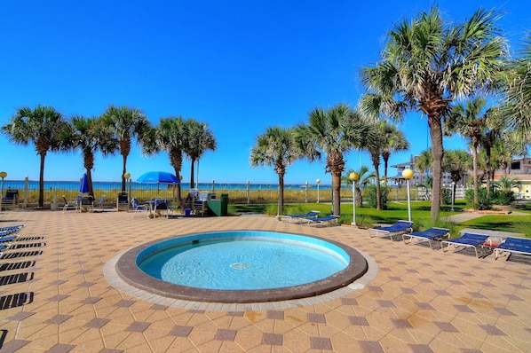 Relax by the resort's central pool, surrounded by lounge chairs and umbrellas, with palm trees nearby.