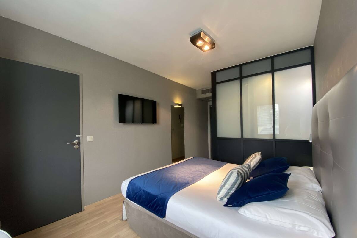 Un dormitorio moderno con cama, televisor montado en la pared y una lámpara de techo.