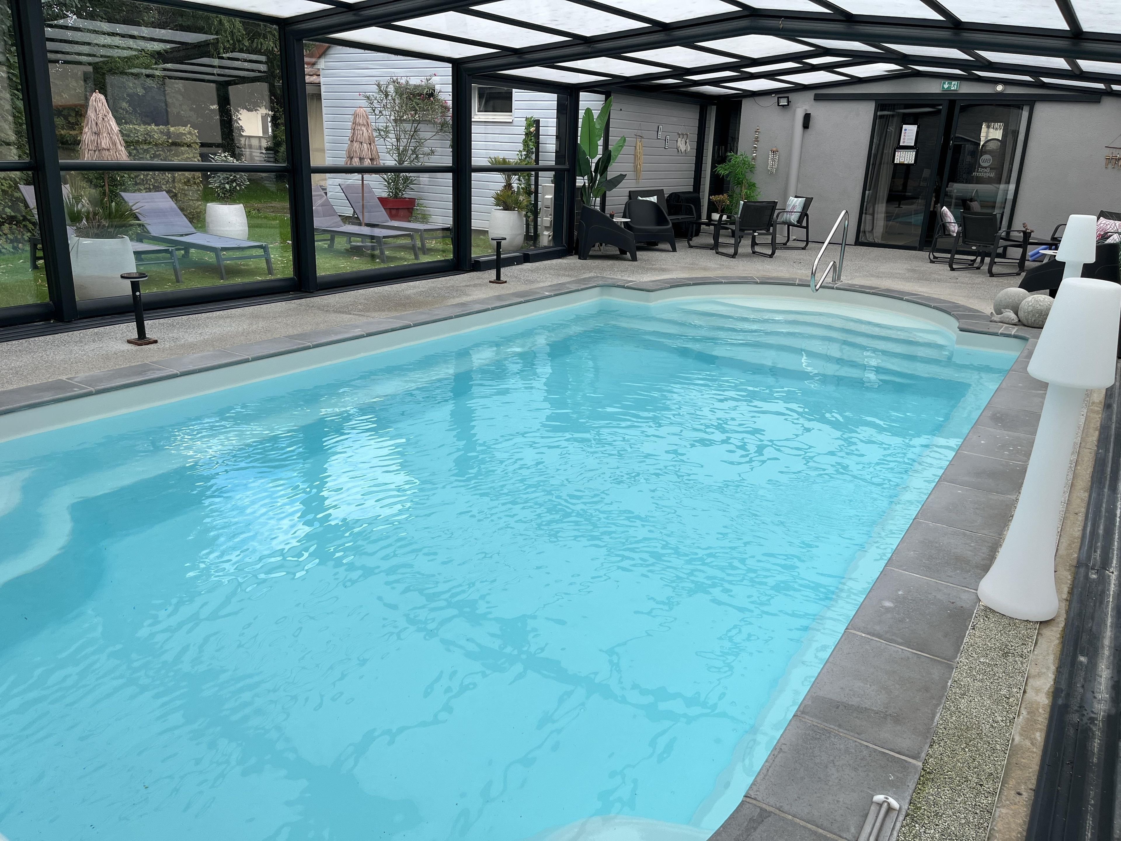 Una piscina interior con sillas de descanso y un cerramiento de vidrio.