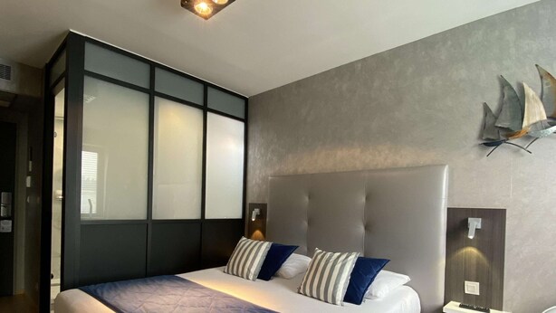 A modern bedroom with a large bed, a headboard, a bedside table, and a wall-mounted light fixture. - Best Western La Mare o Poissons (Ouistreham)