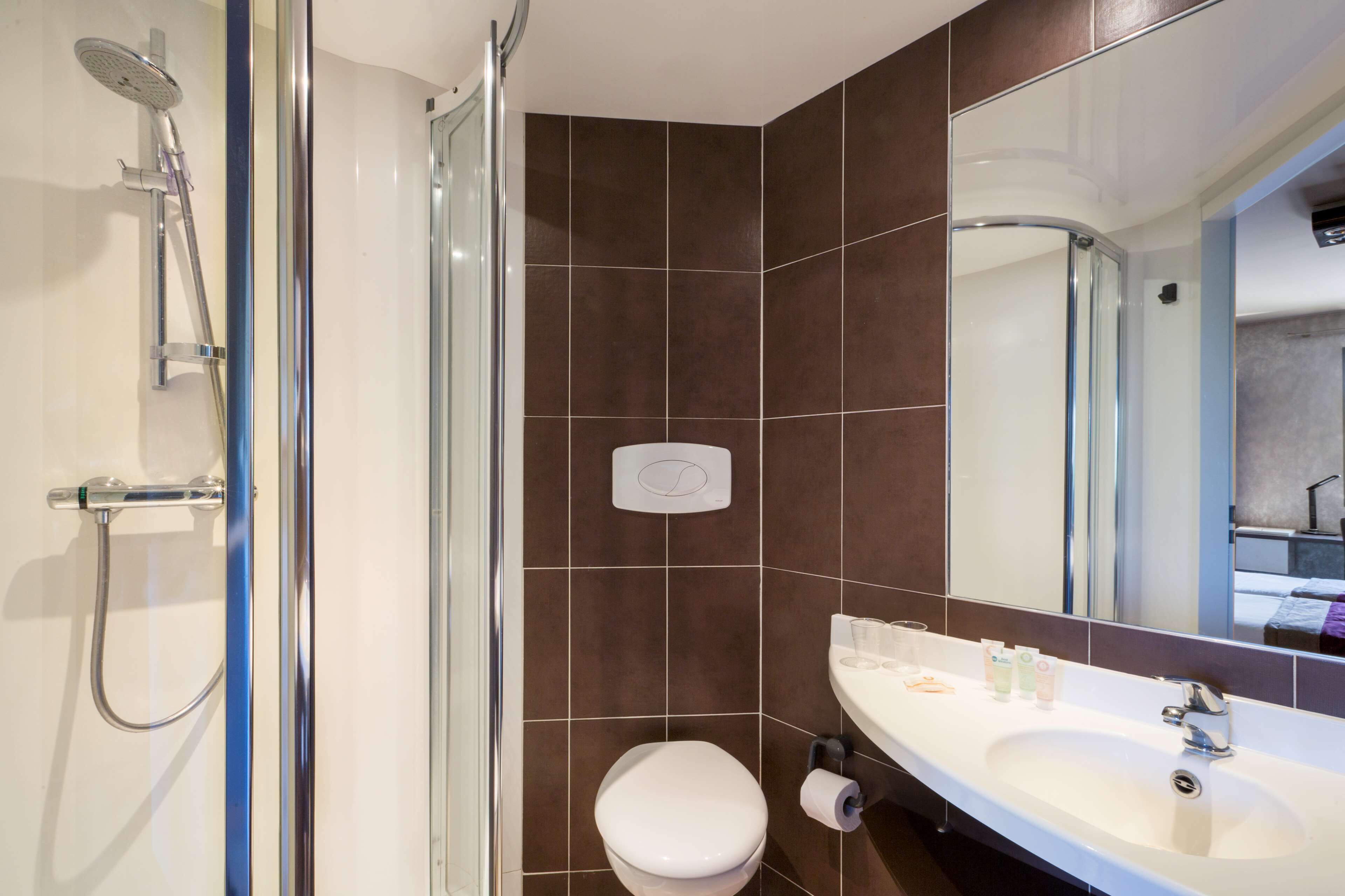 Baño con ducha, inodoro, lavamanos y espejo.