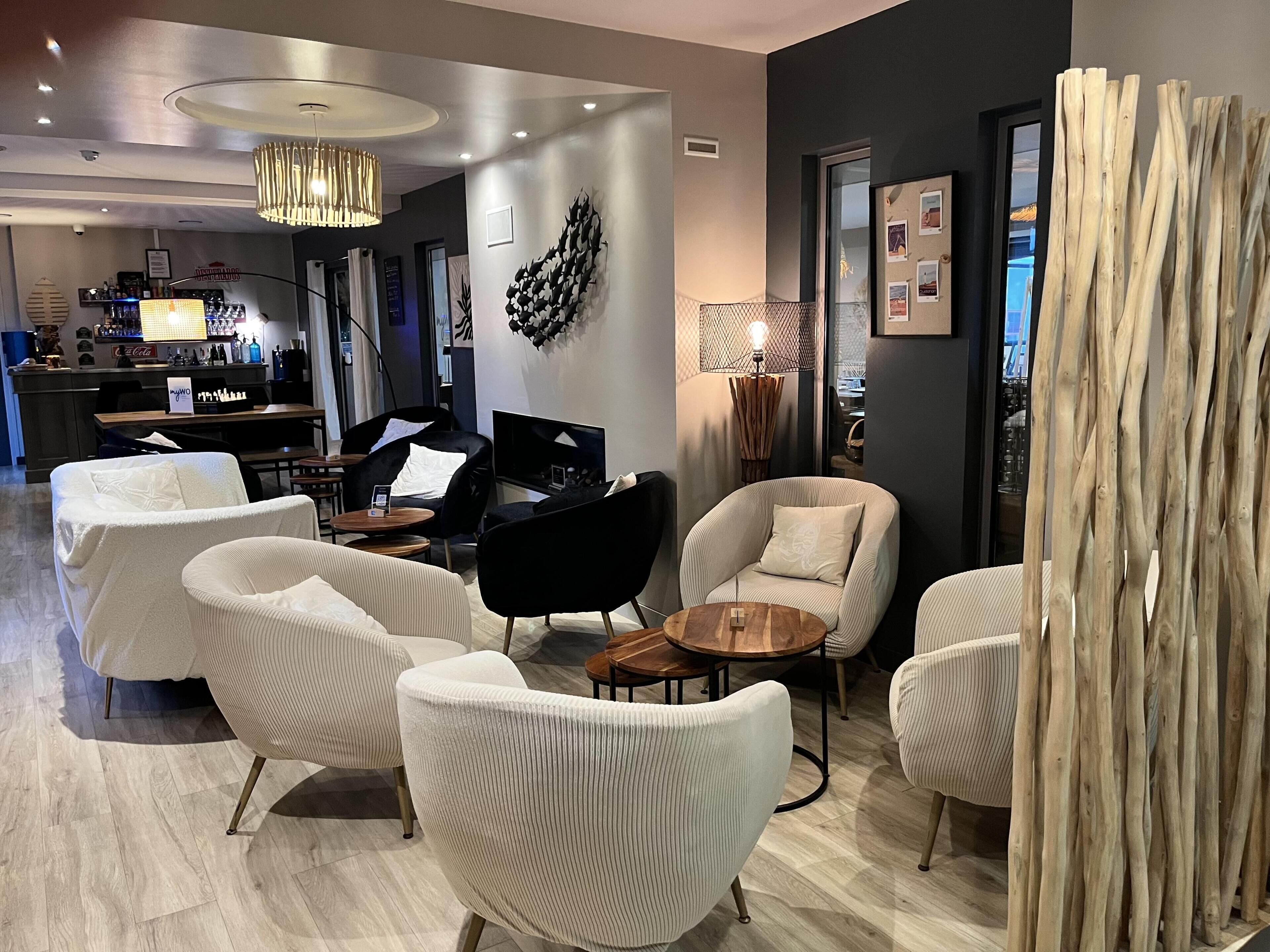 Un espace de détente moderne avec des fauteuils blancs à revêtement, un fauteuil noir, une table ronde en bois et un élément décoratif mural.