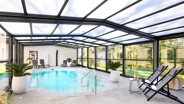 Una piscina interior con techo de cristal, sillas de descanso y plantas en macetas.