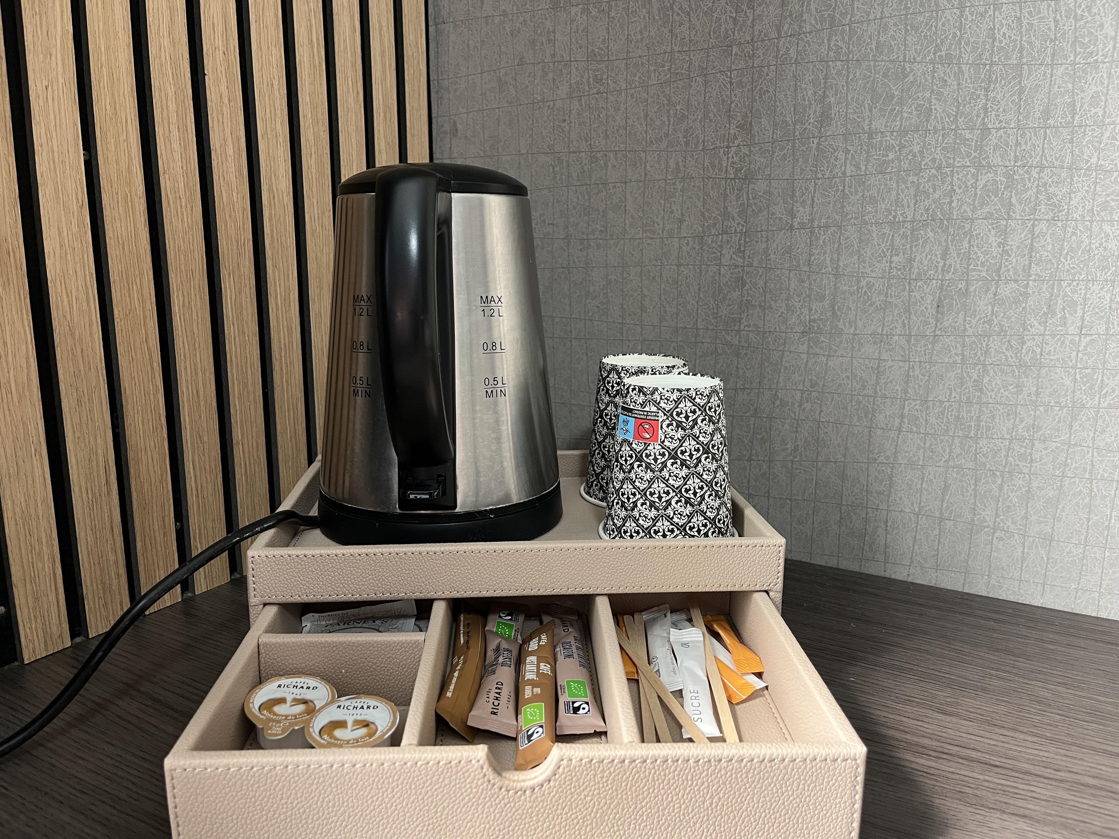 Une machine à café, une tasse à motifs et un tiroir contenant divers objets, notamment des dosettes de café et une cuillère.
