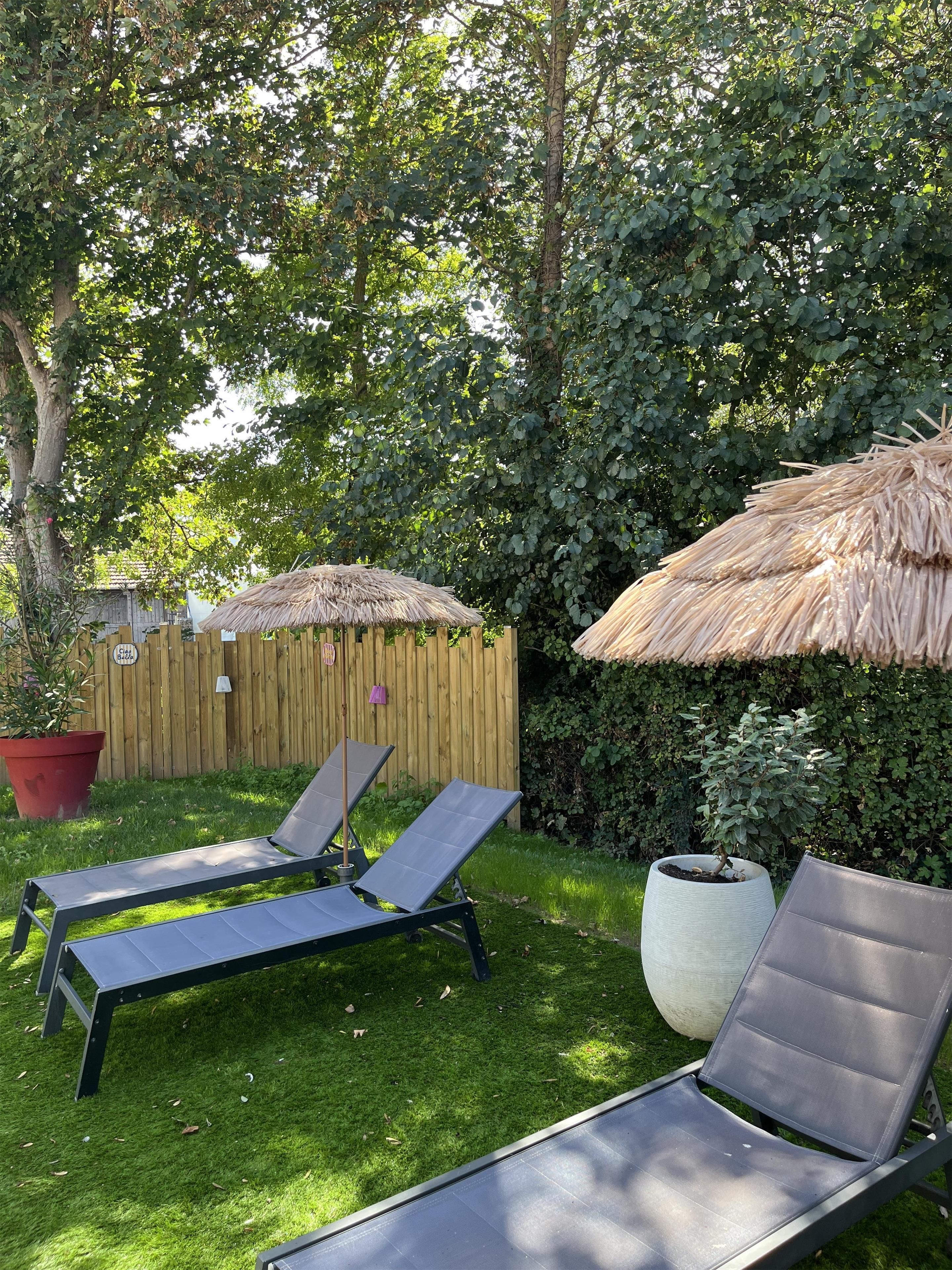 Two lounge chairs with thatched umbrellas in a garden setting.