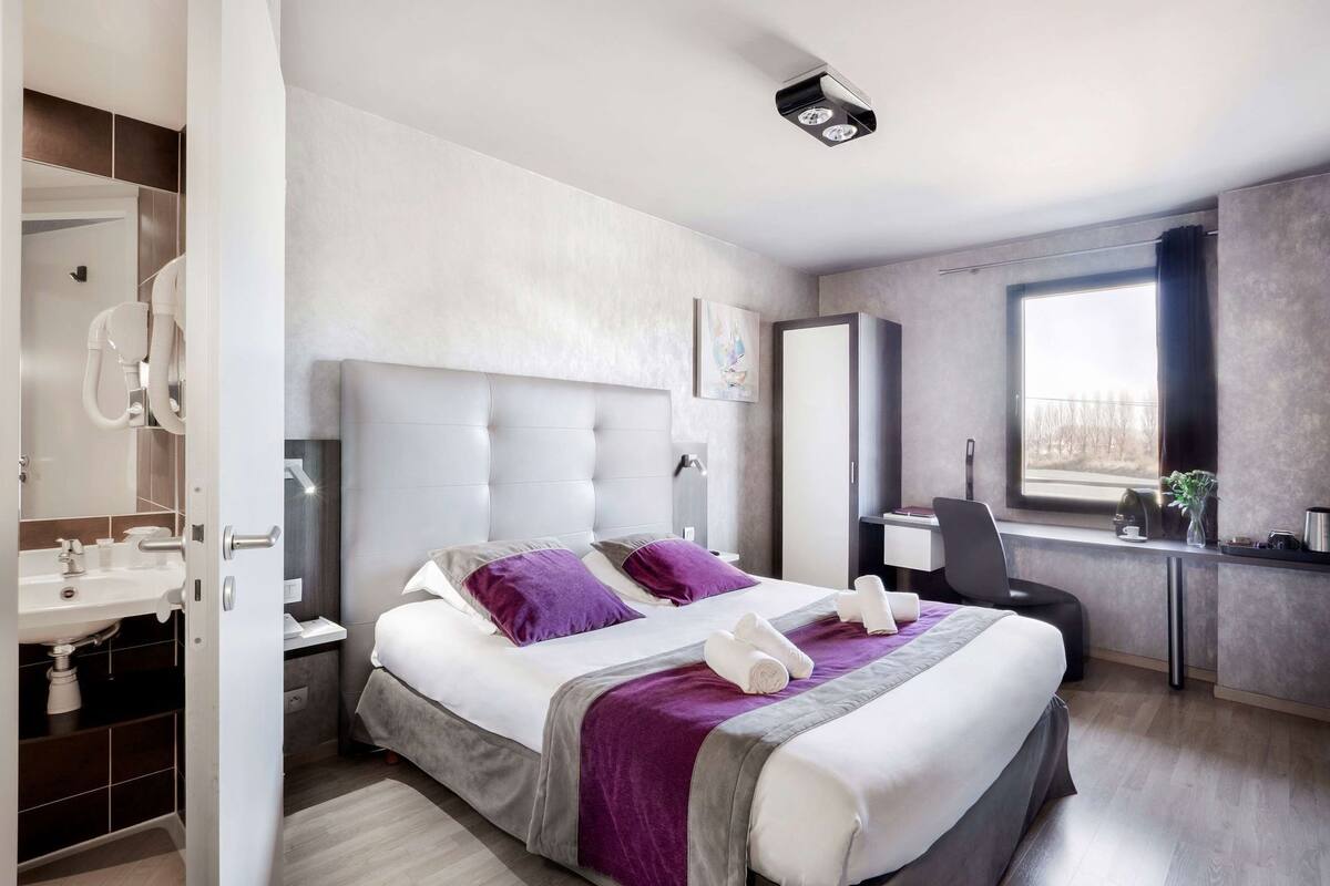 Una habitación de hotel moderna con una cama grande, un escritorio, una ventana y un baño.