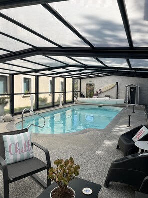 Ein Poolbereich mit Glasdach, einem kleinen Innenpool und Liegestühlen.