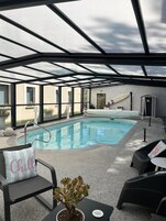Un área de piscina con techo de cristal, una piscina interior pequeña y sillones de descanso.